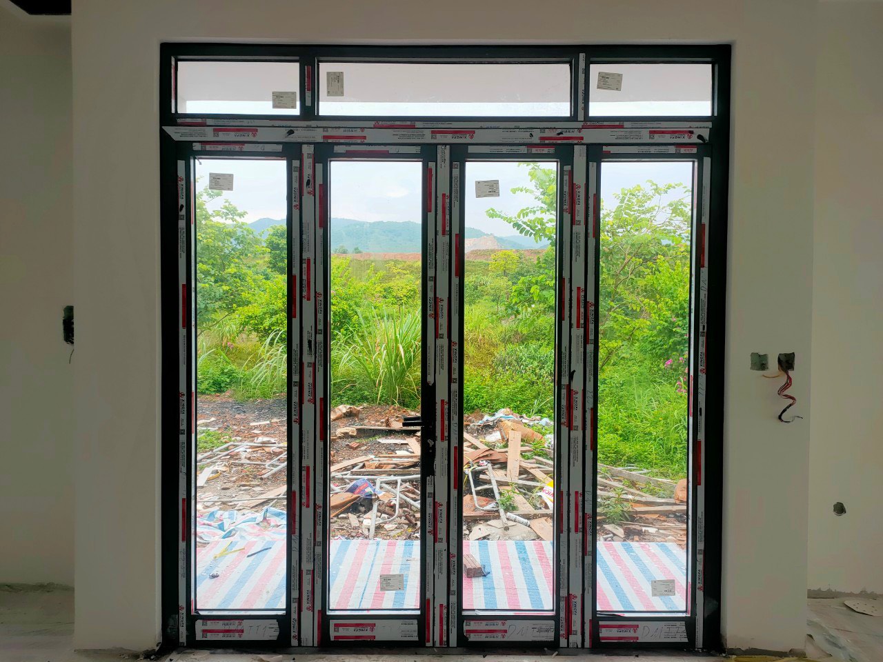 Cửa nhôm kính 4 cánh khung đen đang lắp đặt, nhìn ra khu vườn cây xanh bên ngoài